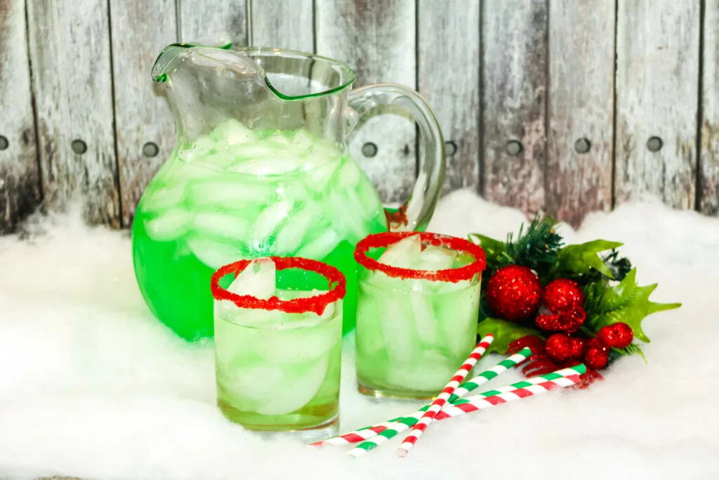 green grinch punch in a pitcher with small glasses filled with punch
