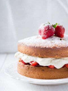 side shot of a sponge cake with strawberries and whipped cream on top