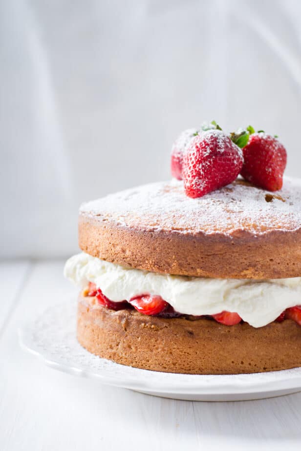 side shot of a sponge cake with strawberries and whipped cream on top