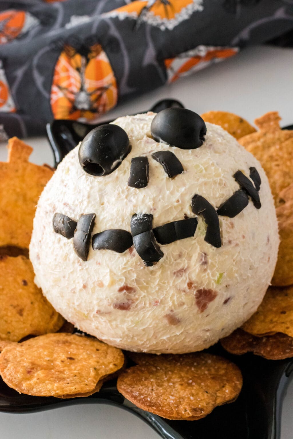 a jack skellington cheese ball on a plate with orange pumpkin shaped chips