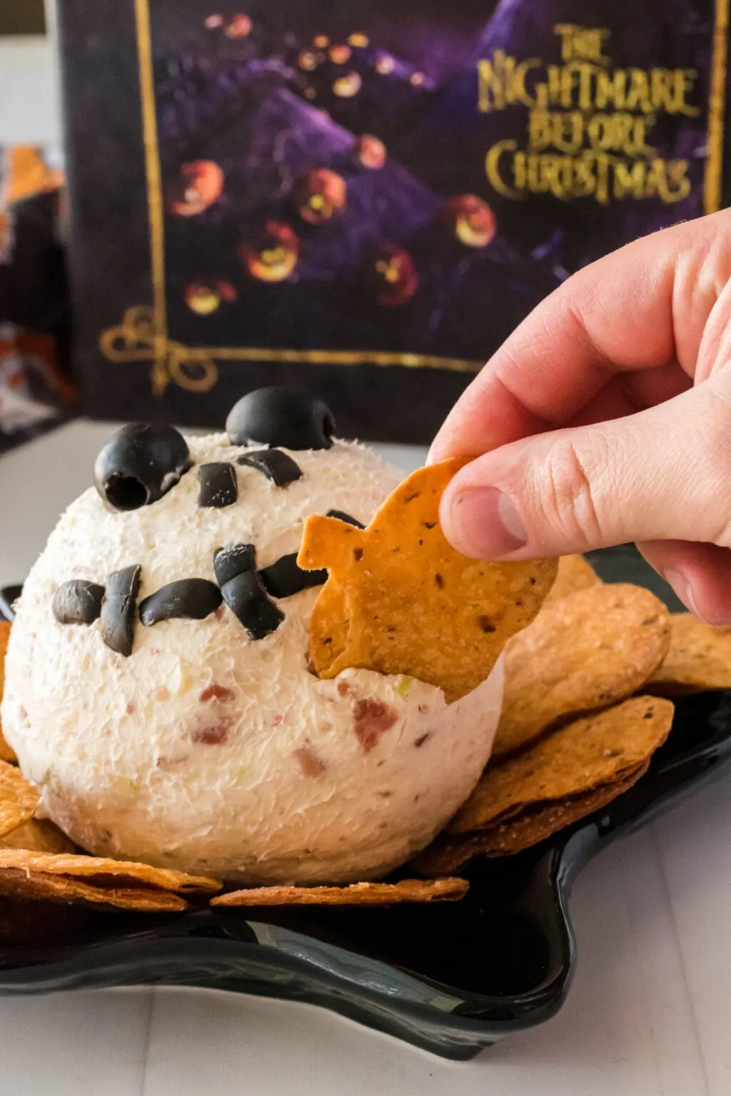 a hand dipping a chip into the side of a cheese ball recipe