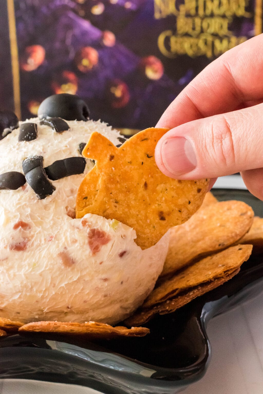 a hand scooping up some cheese ball onto a pumpkin shaped chip