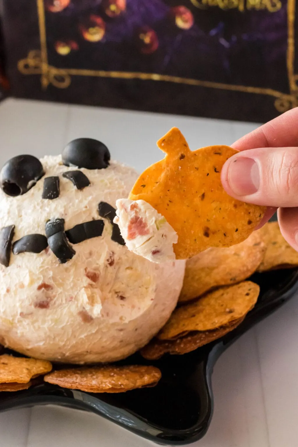 A hand dipping a pumpkin chip into a jack skellington cheese ball
