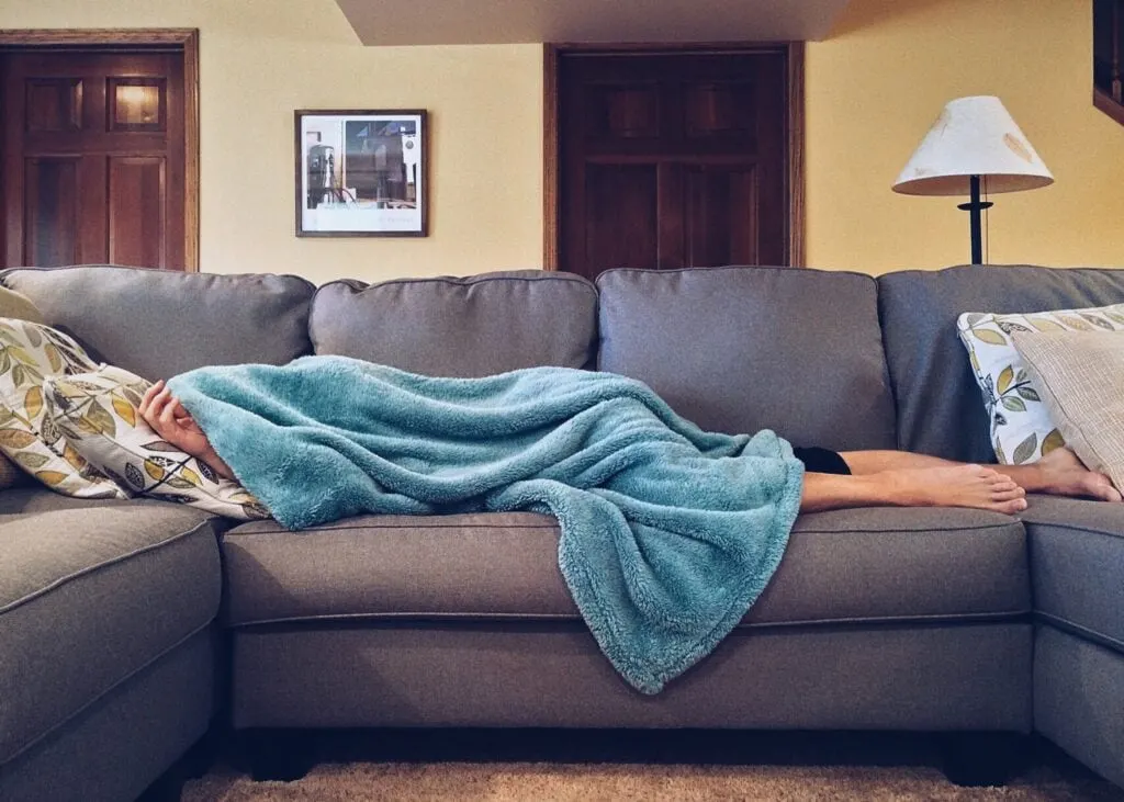 a person asleep on the couch with a blanket pulled over them