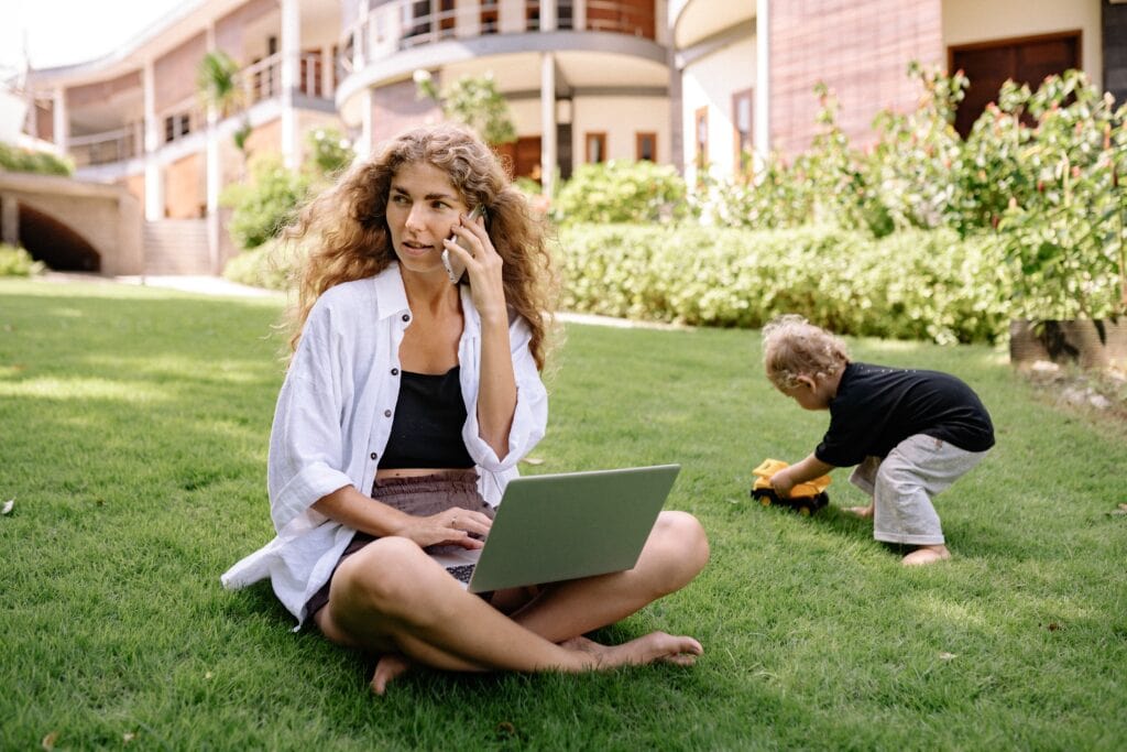 woman on a computer and the phone while kid playing aside her