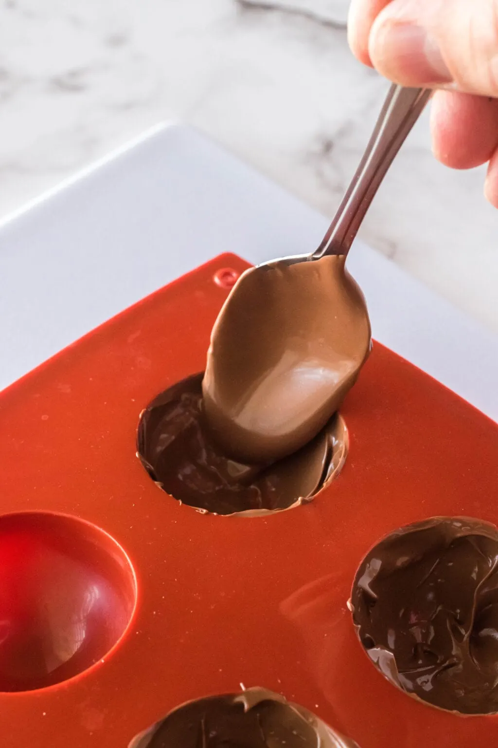 spoon putting melted chocolate into a silicone mold