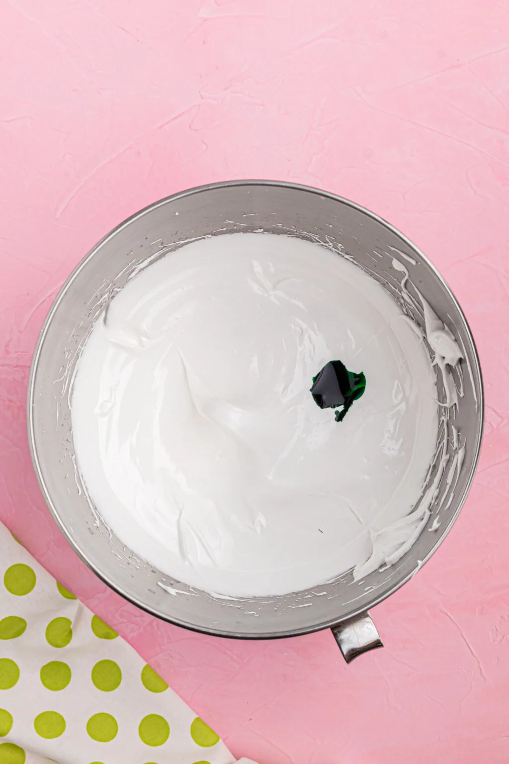white meringue mixture in bowl with green food coloring drops