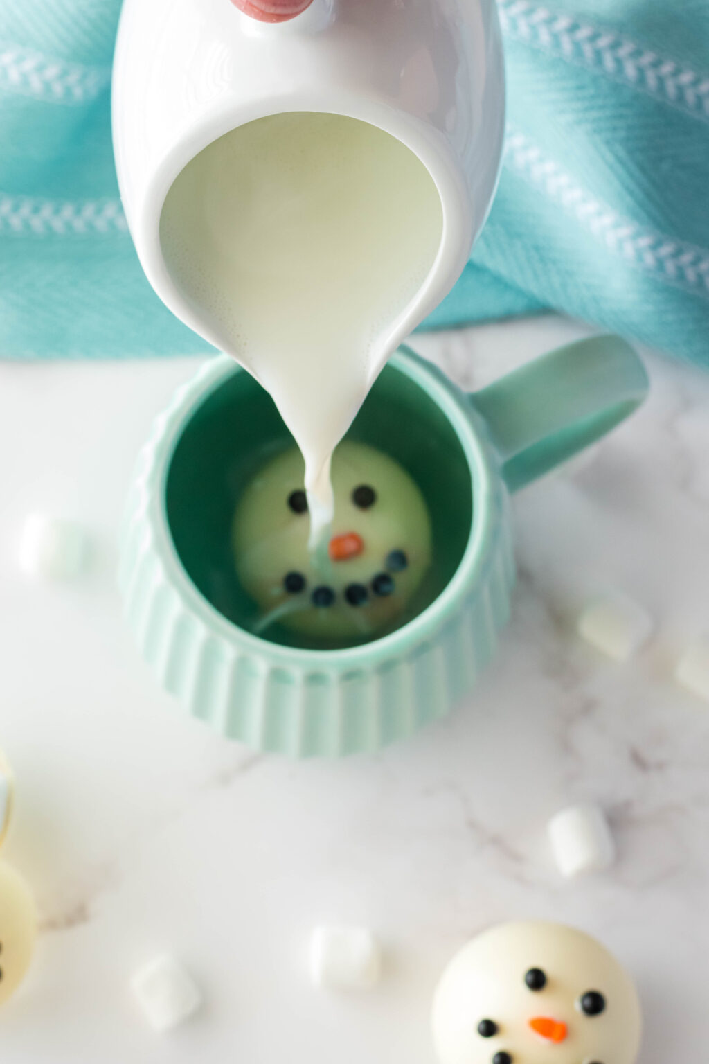 hot milk being poured into a mug with a snowman hot cocoa bomb inside