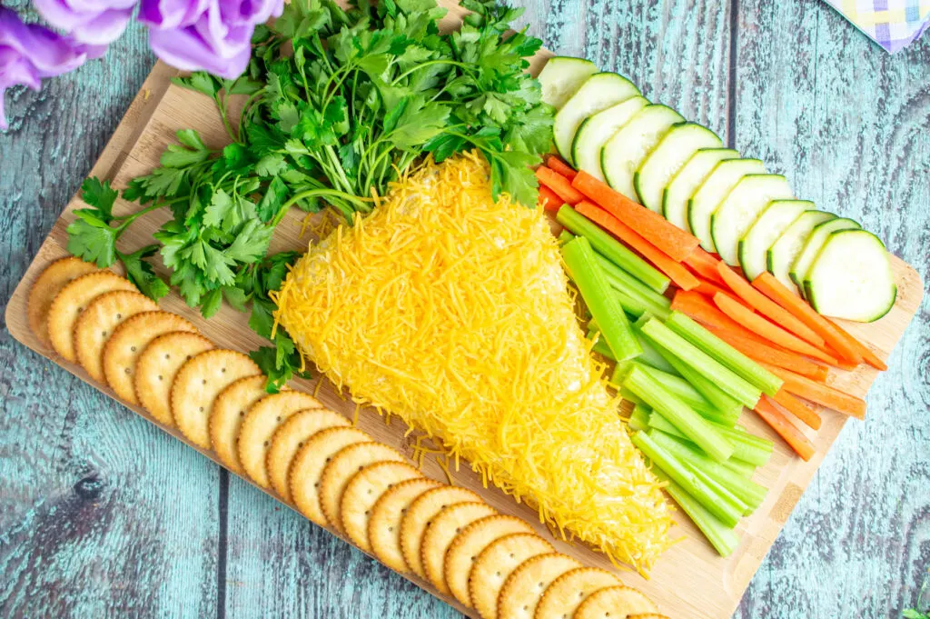 easter carrot cheese ball on cutting board with vegetables and crackers around it