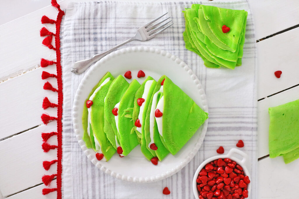 green grinch crepes with white cream cheese filling and red heart sprinkles on a white plate