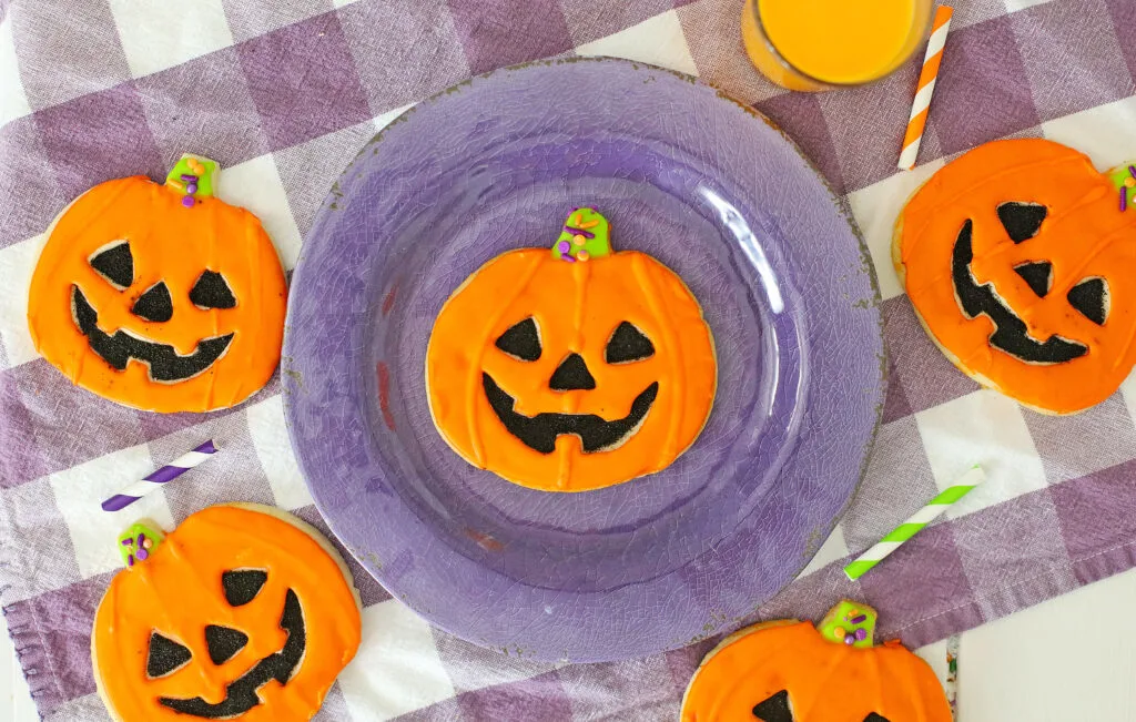 jack-o'-lantern cookies decorated to look like pumpkins on a purple plate