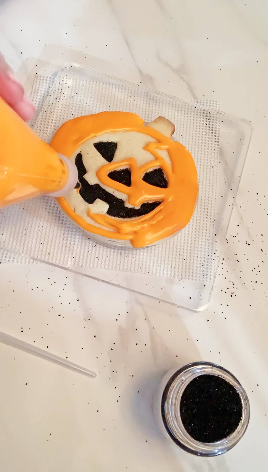 hand piping orange frosting onto baked jack o lantern cookie