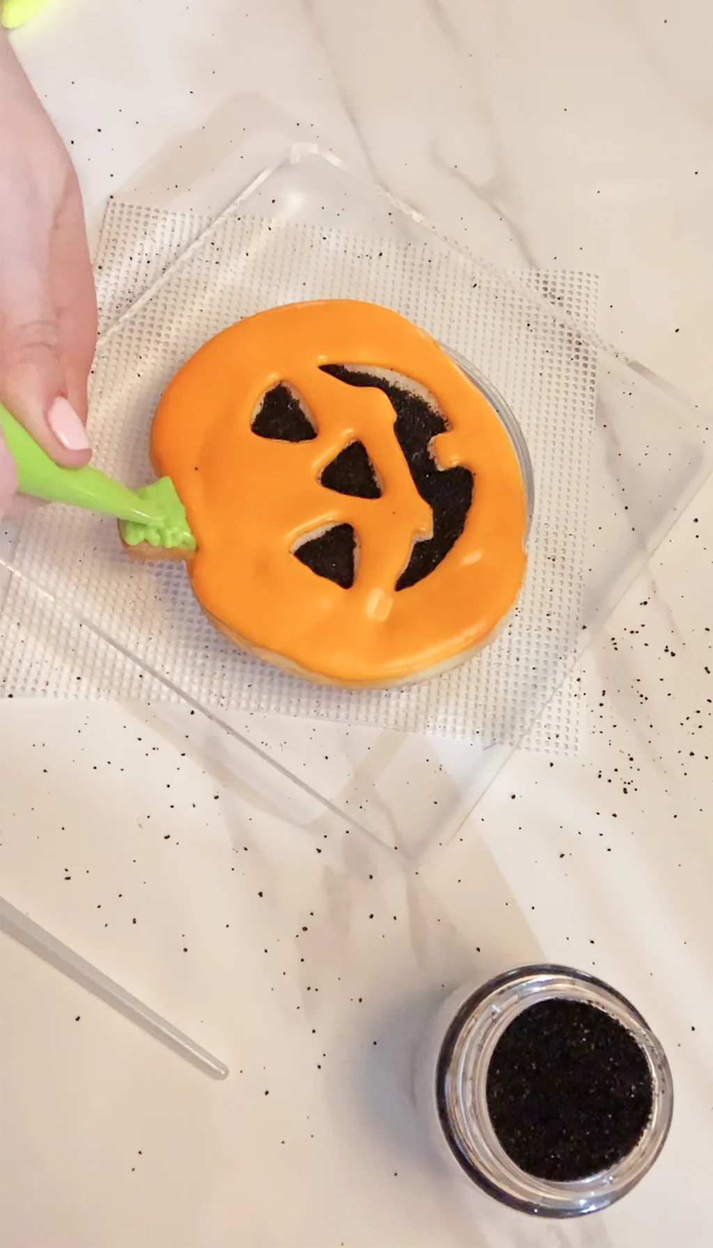 hand piping green frosting onto baked jack o lantern cookie
