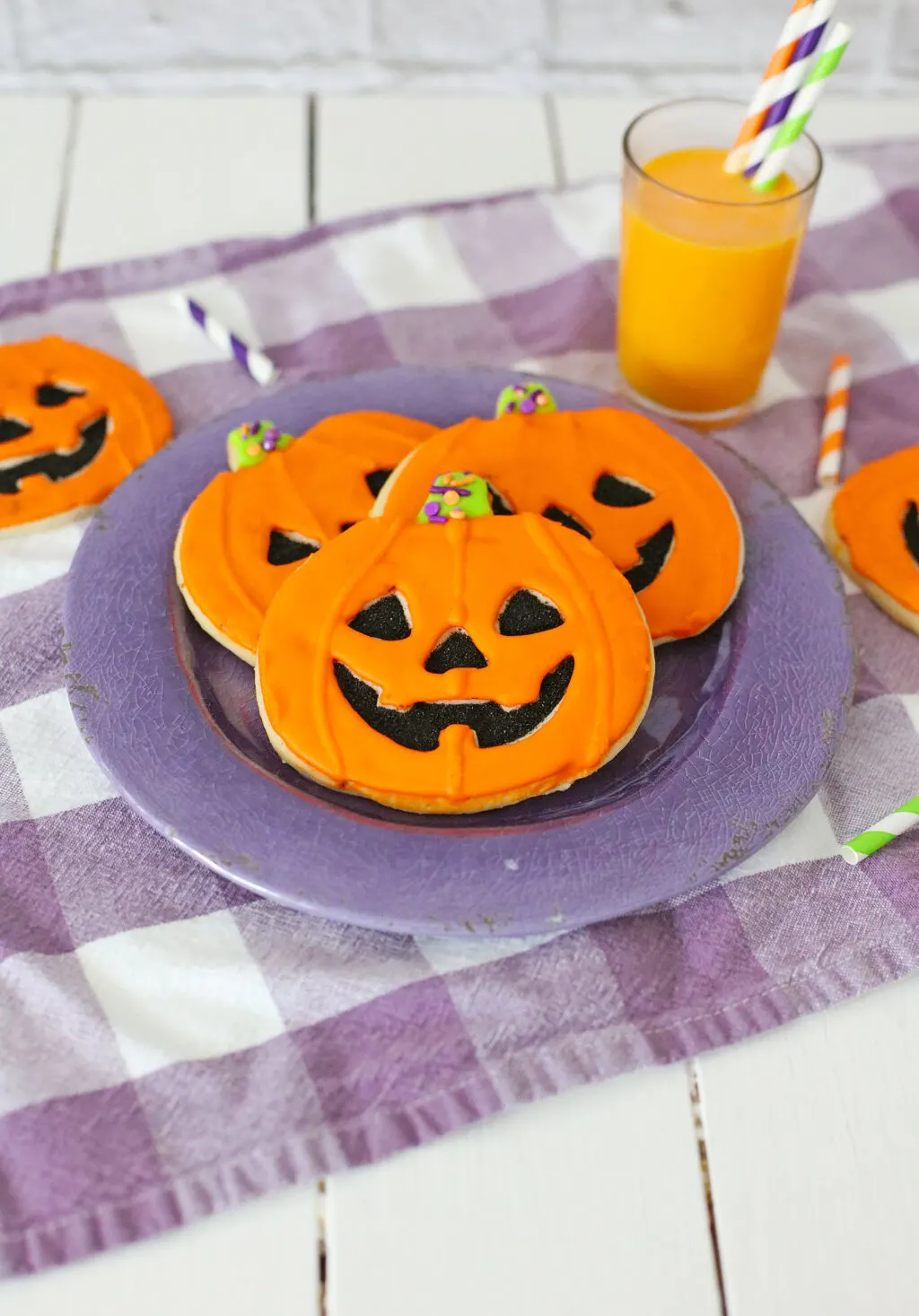 jack-o'-lantern cookies decorated to look like pumpkins on a purple plate