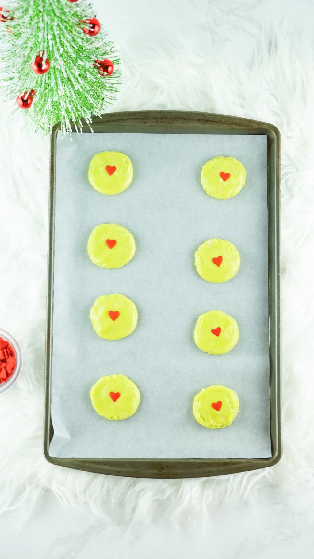 green cookie dough with red heart sprinkles on a baking sheet