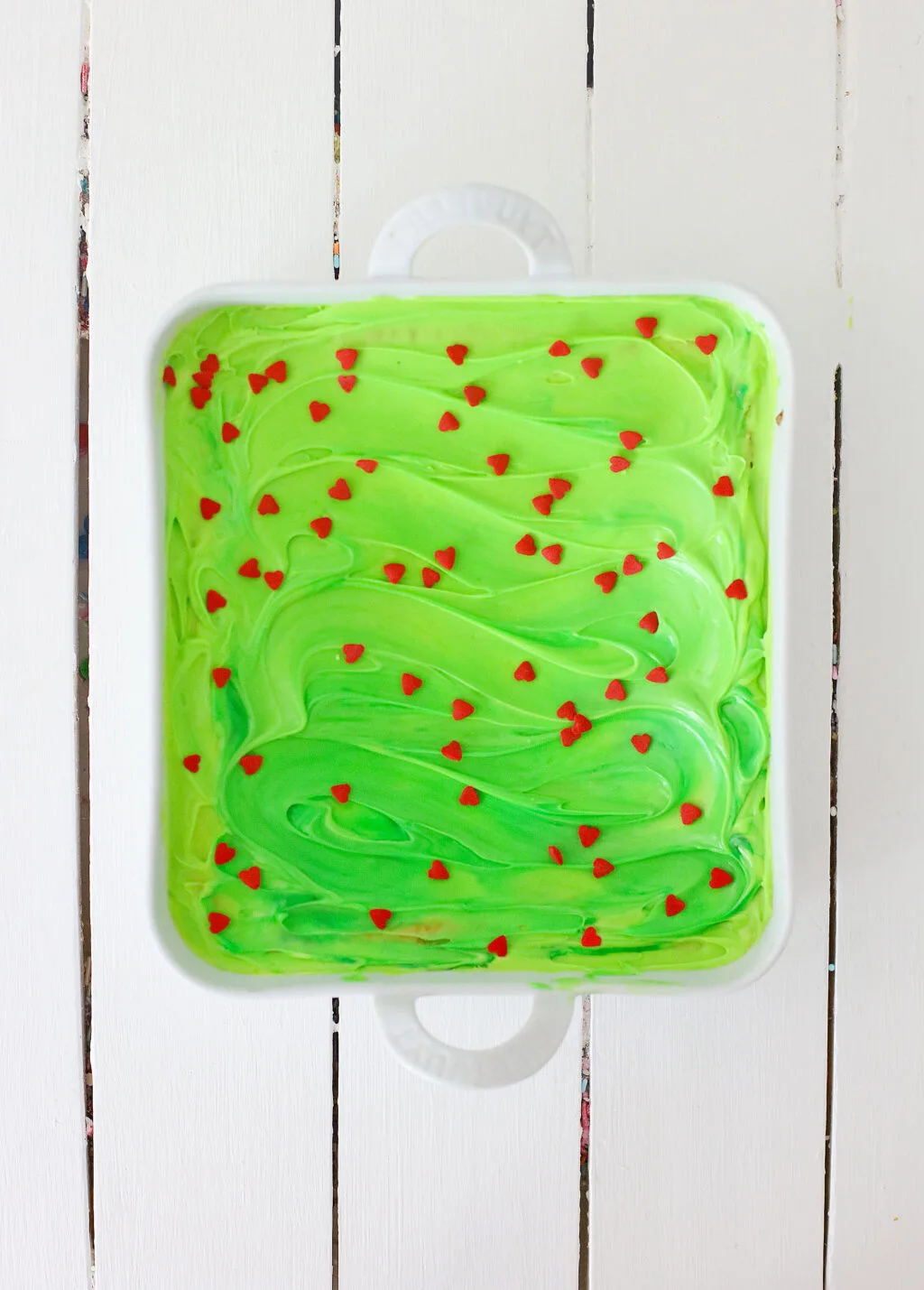 grinch brownies covered in green frosting and red heart sprinkles in a pan