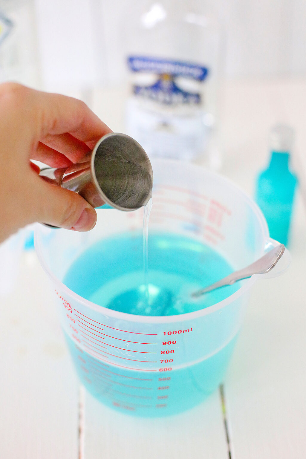 woman's hand pouring vodka into a cup of blue mixture