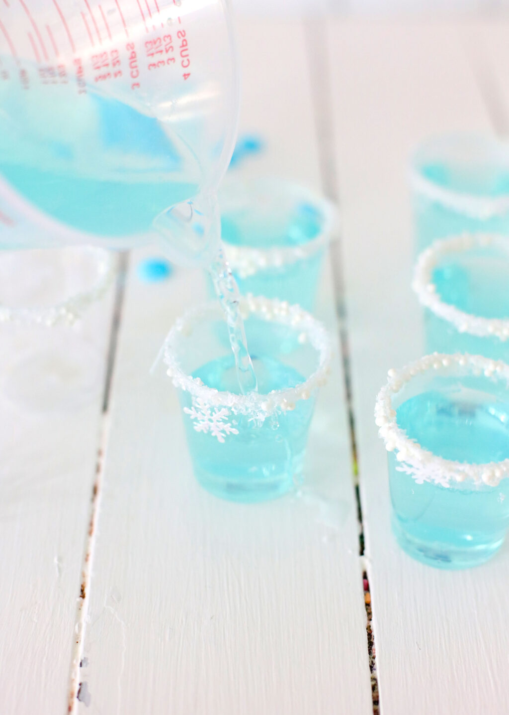 measuring cup pouring bright blue mixture into plastic jello shot cups