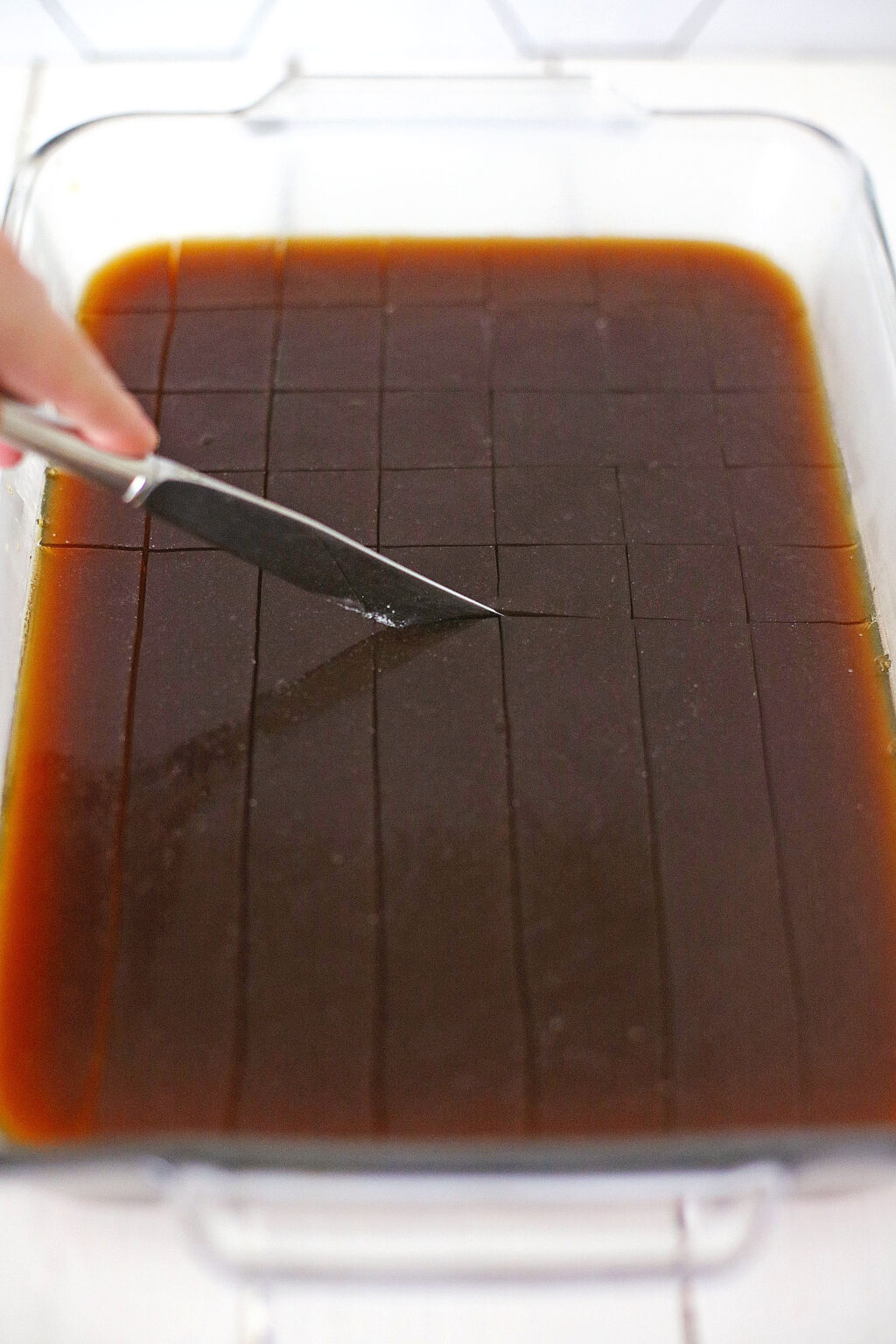 woman cutting coffee jelly into small squares using butter knife