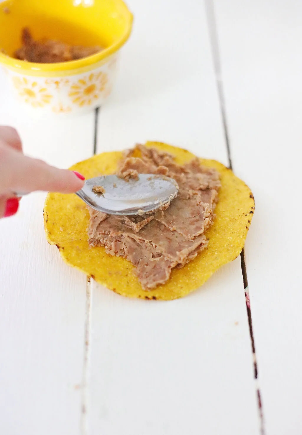 woman spreading refried beans onto top of tostada shell