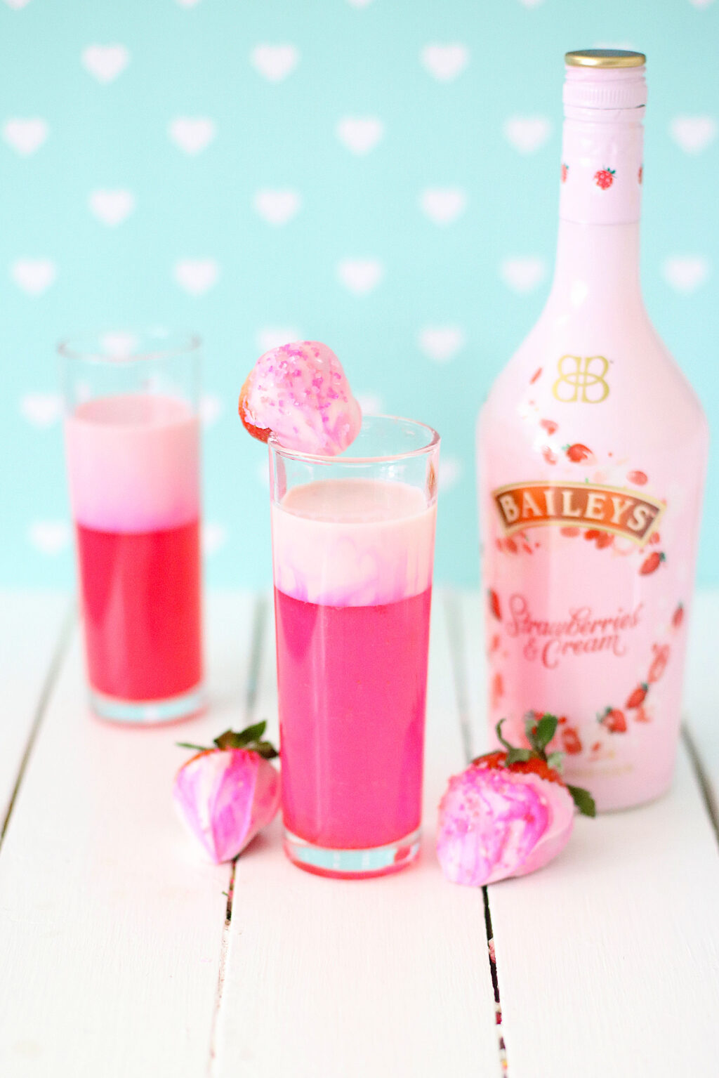 shimmery pink cocktail in clear glass with strawberries next to it