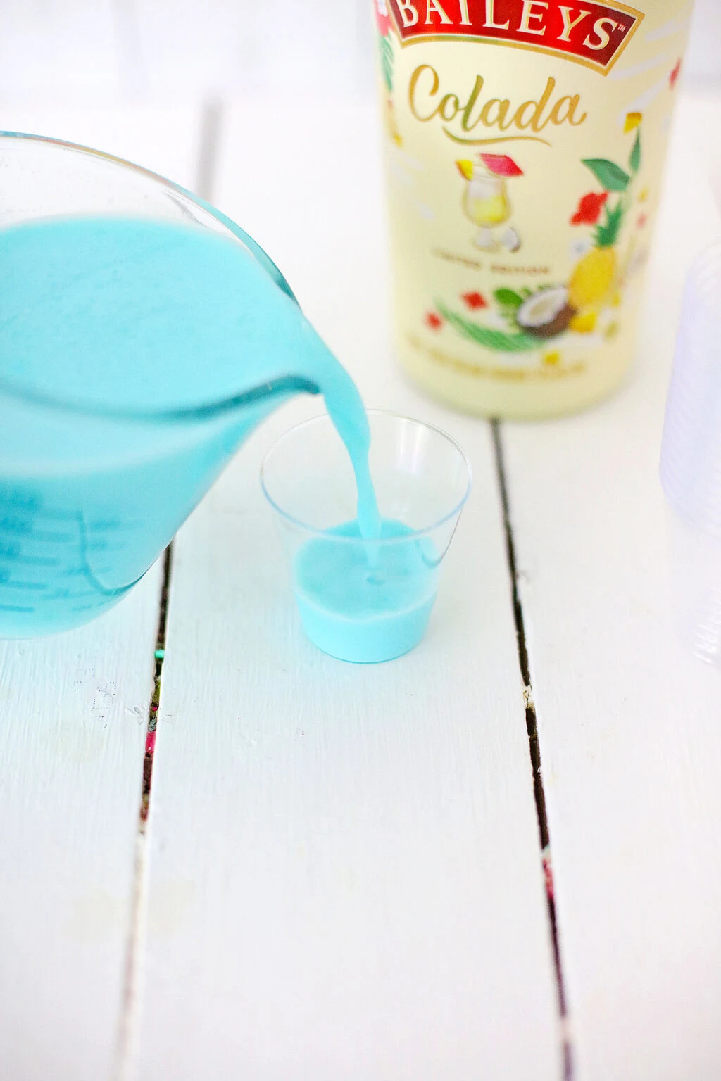 aqua jello shot mixture being poured into small plastic jello shot cup