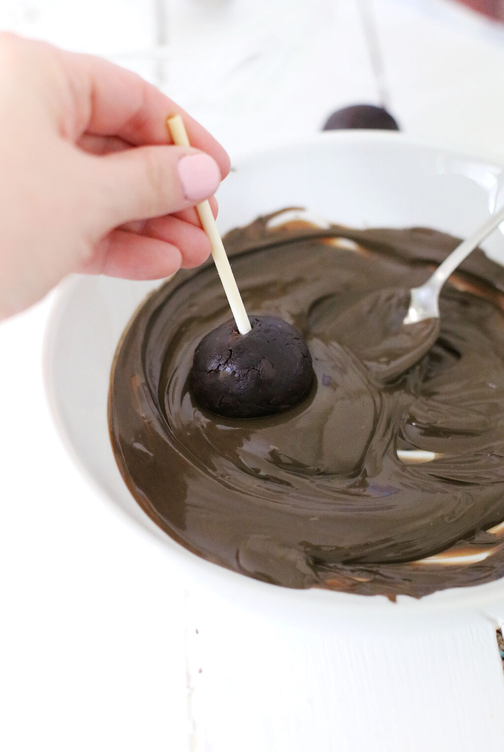 chocolate cake pop being dipped into melted chocolate
