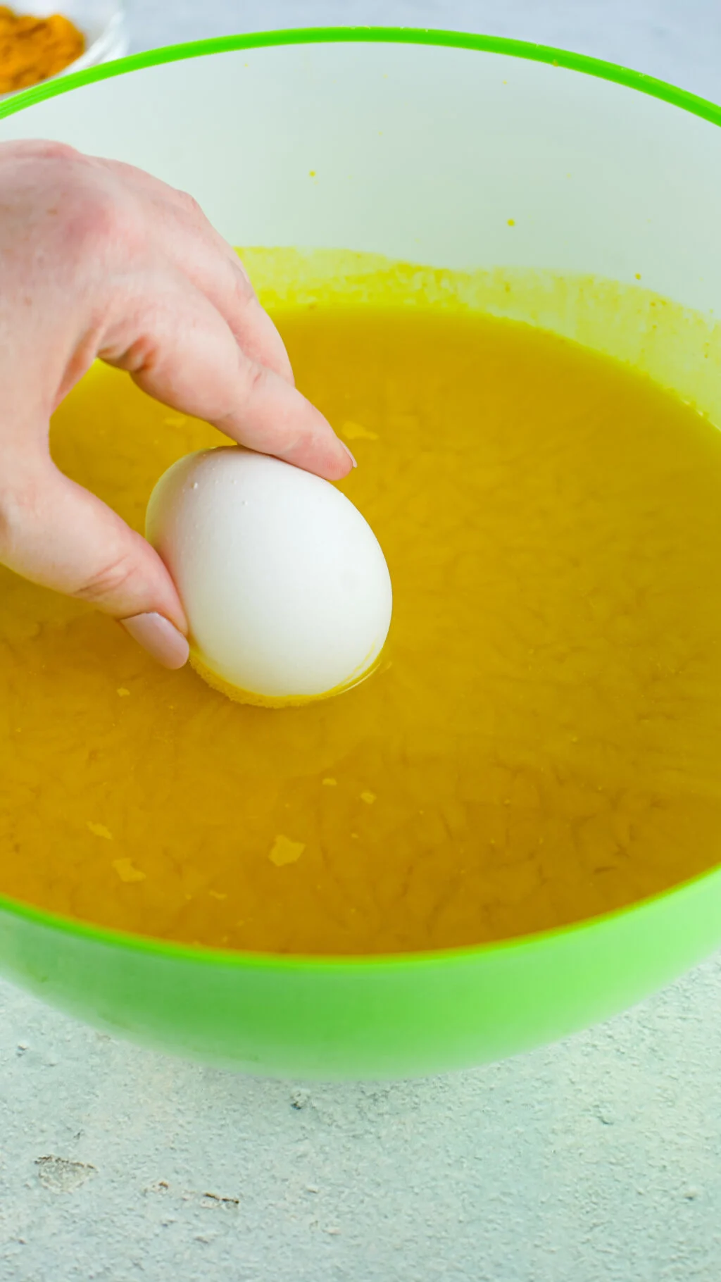 woman's hand placing a hard boiled egg inside a turmeric water bowl