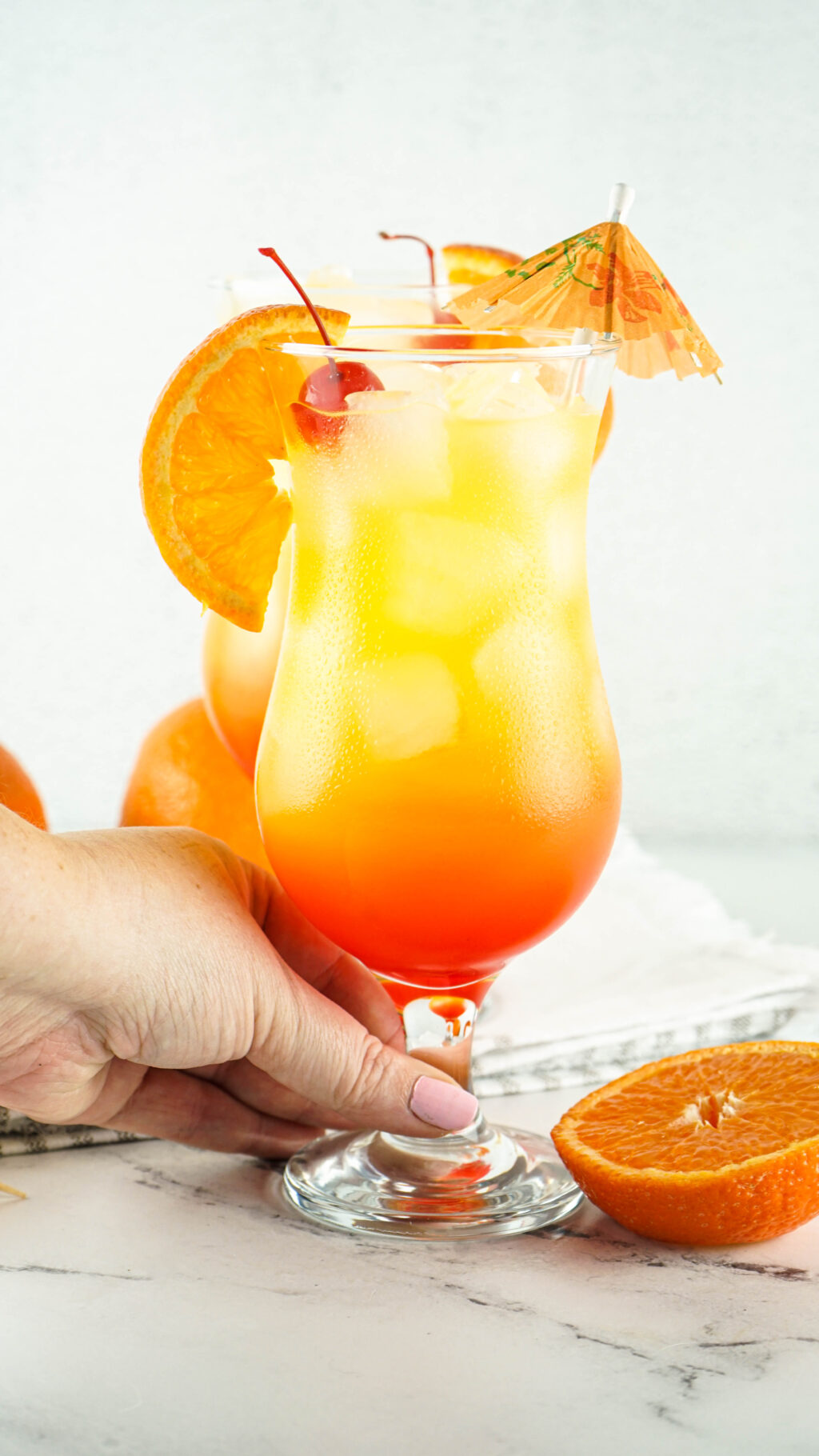 woman's hand holding a tequila sunrise cocktail in a hurricane glass