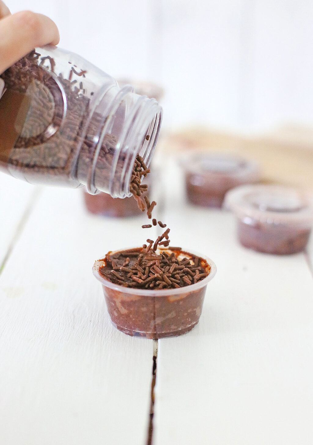 chocolate sprinkles being poured on top of chocolate pudding shots