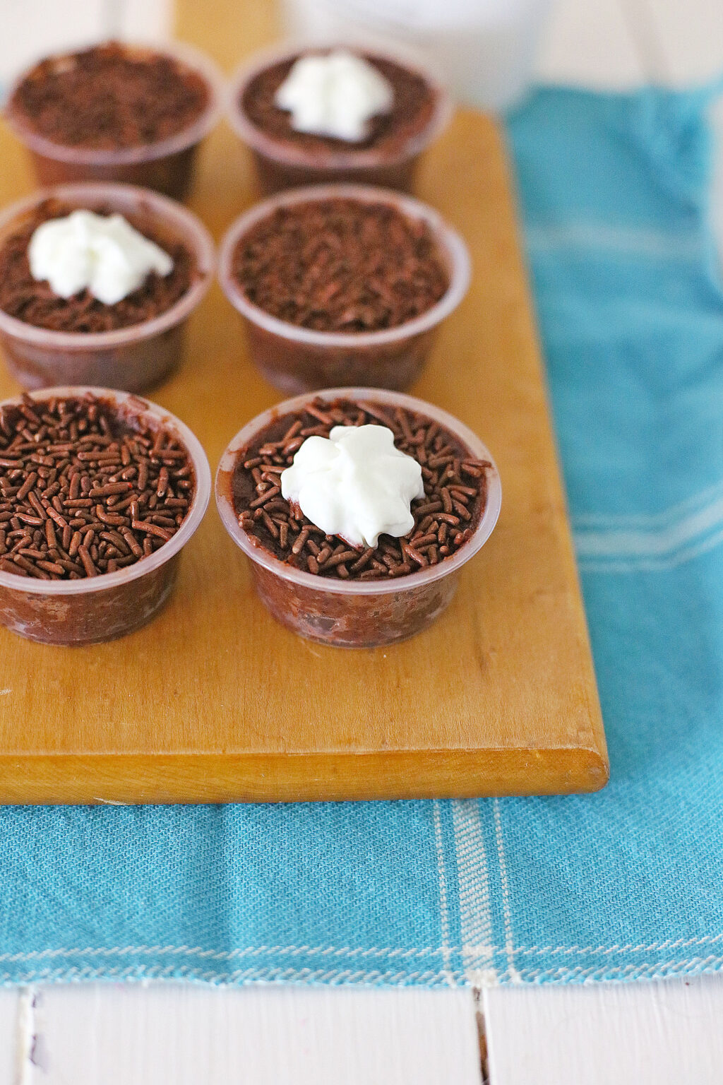 chocolate pudding shots with whipped cream on top on a cutting board