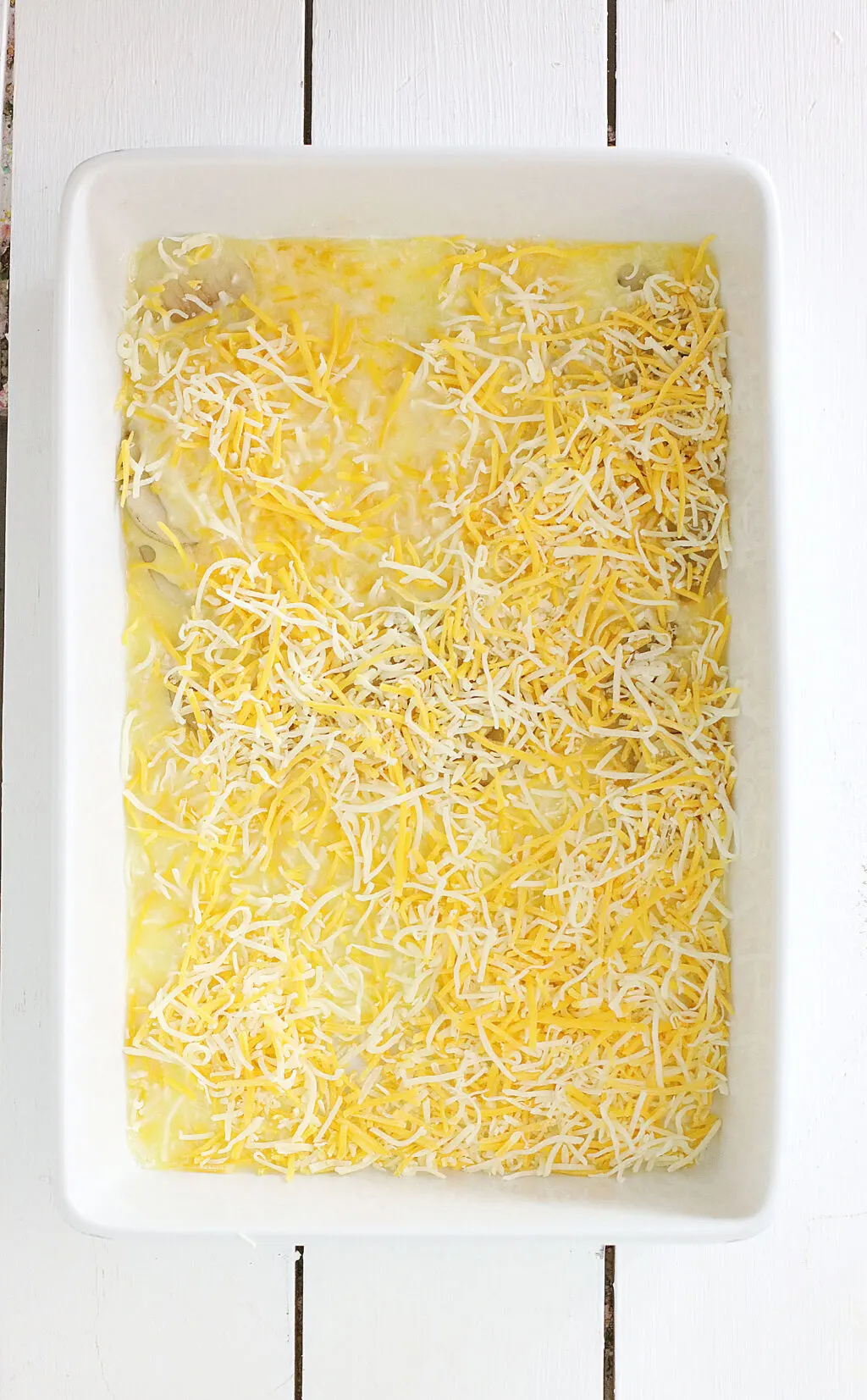 shredded cheese sprinkled on top of potatoes in casserole dish