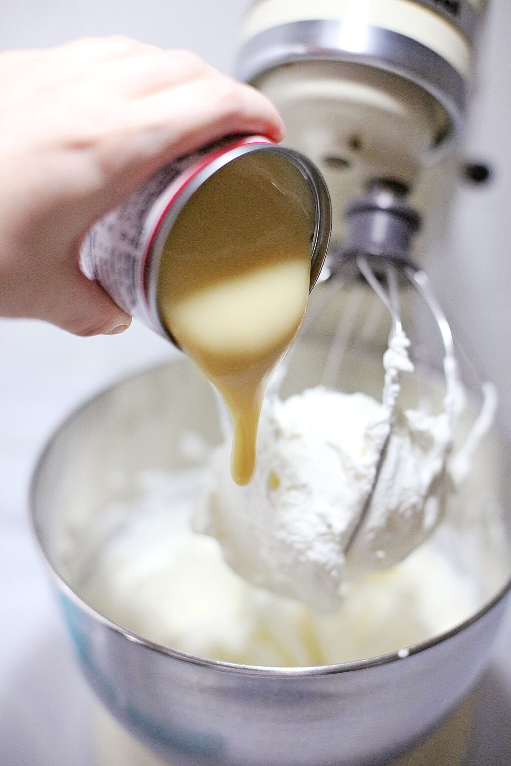 can of sweetened condensed milk being poured into mixing bowl