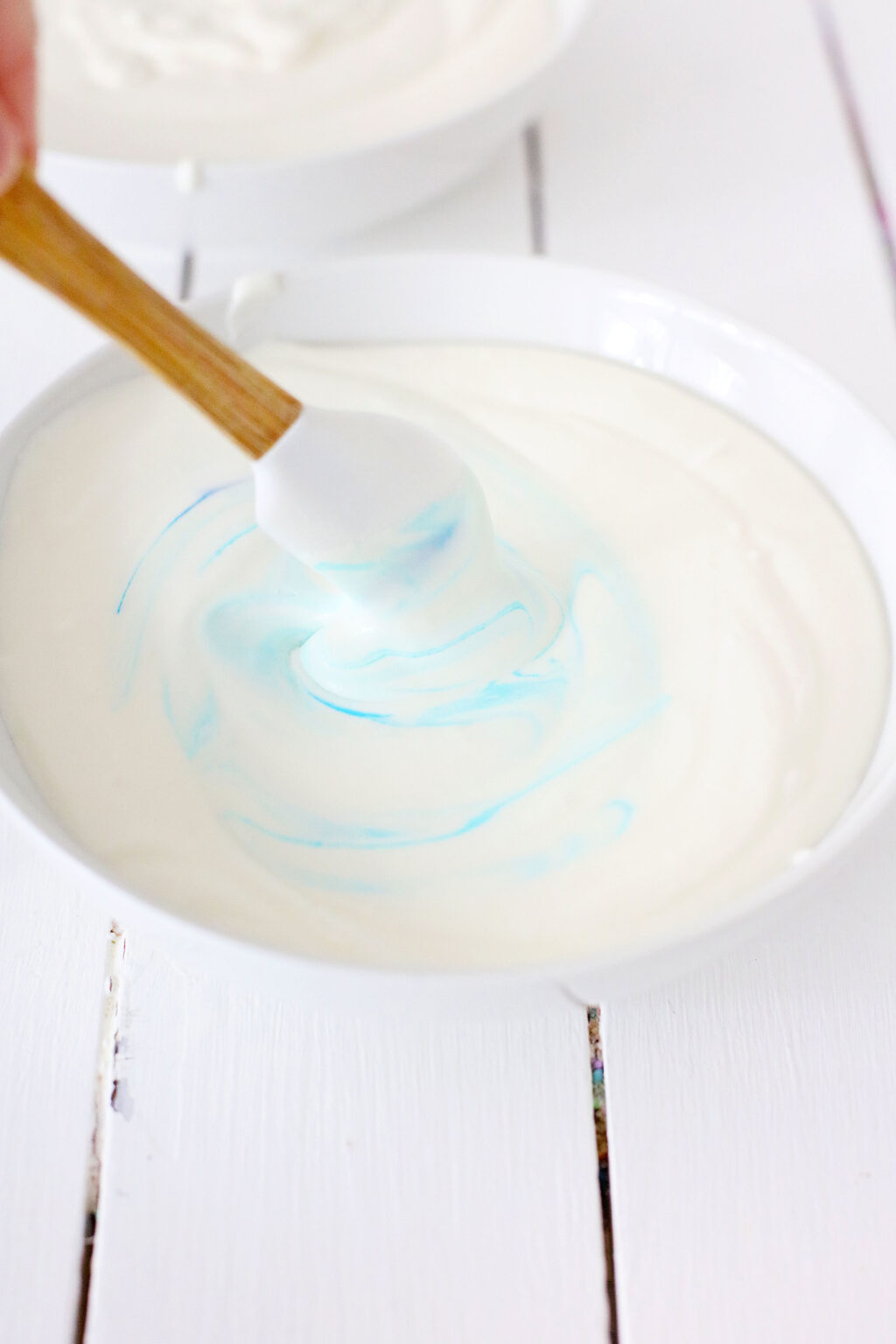 blue food coloring being mixed into ice cream mixture in large bowl