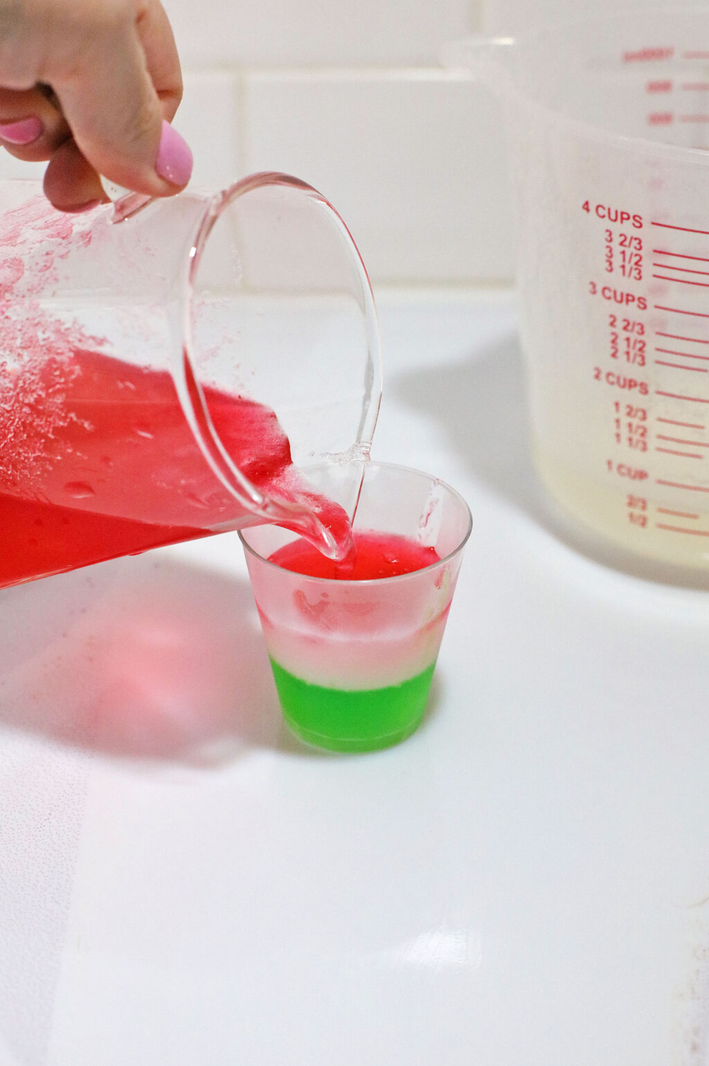 pink gelatin mixture being poured into shot glass
