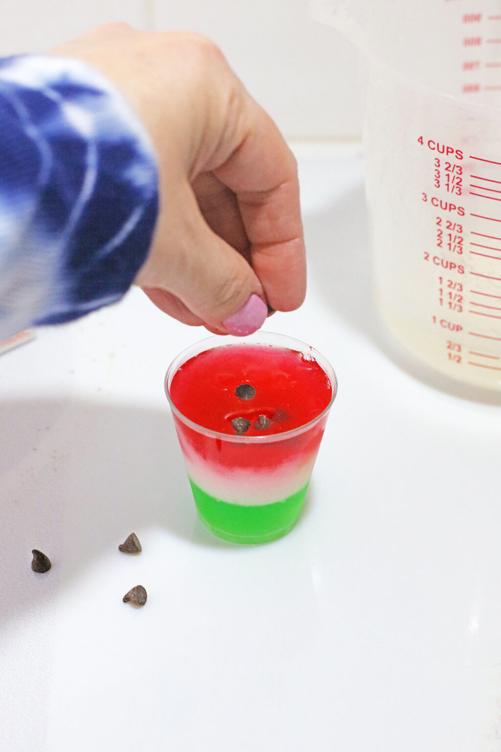 woman's hand placing mini chocolate chips on top of watermelon jello shots