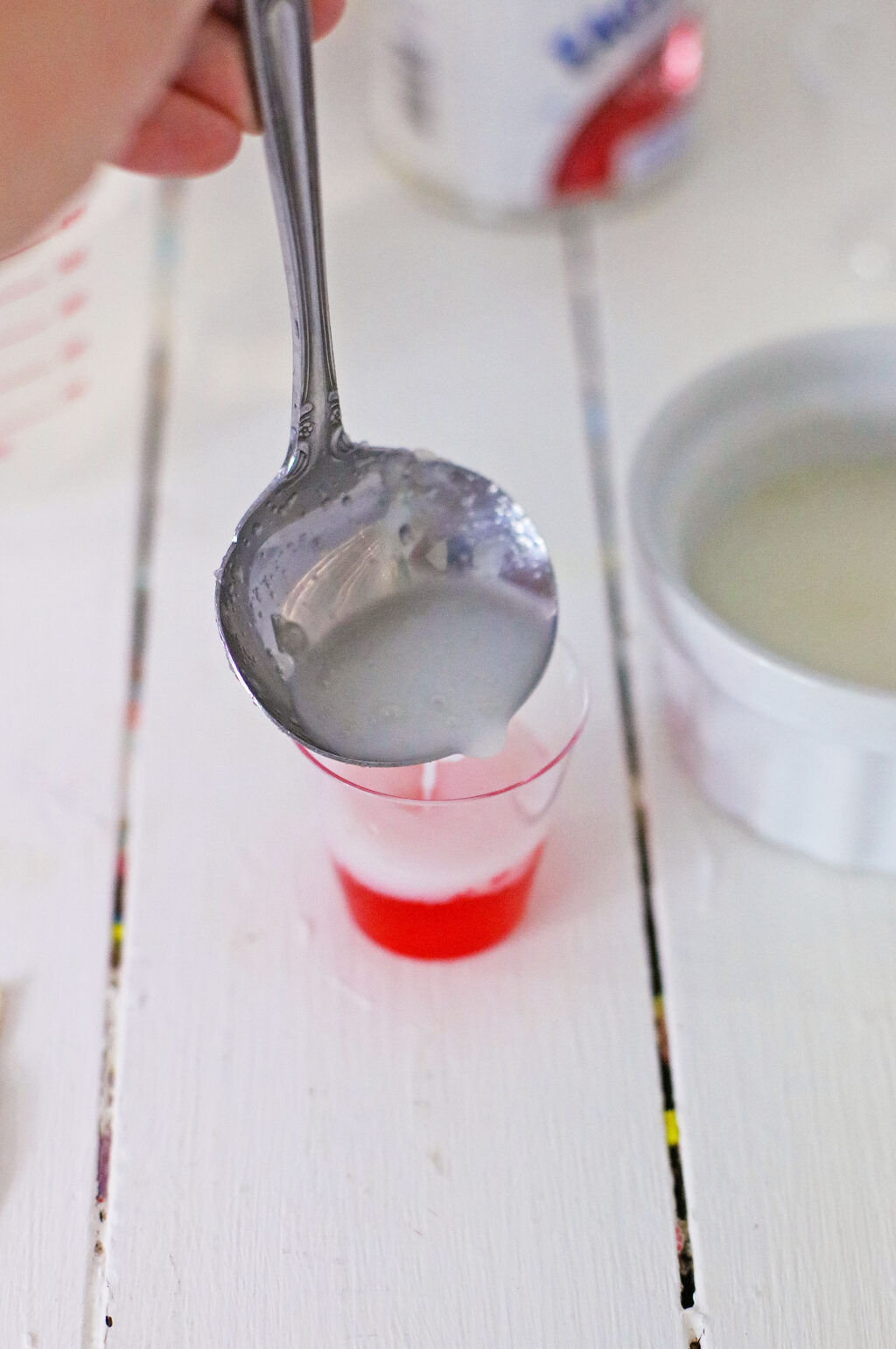 white layer of jello being poured into red jello shot glass