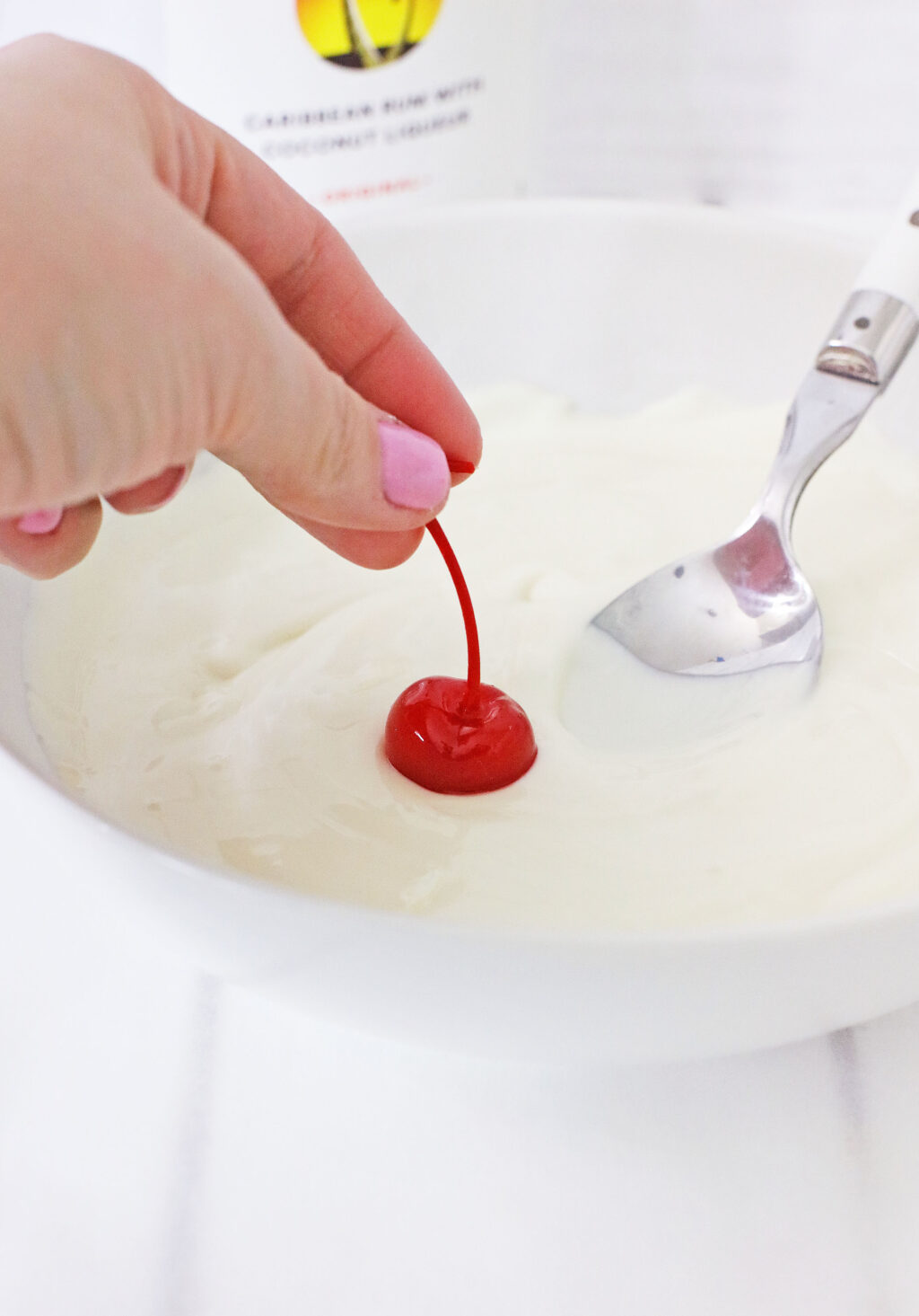 woman's hand dipping red cherry into white melted chocolate