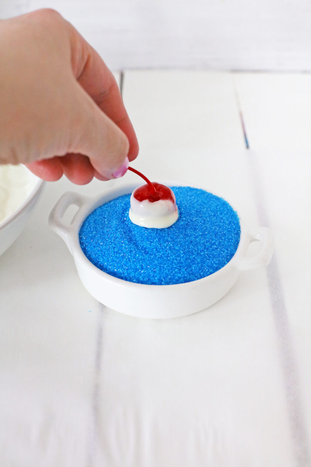 woman's hand dipping chocolate dipped cherry into blue sprinkles