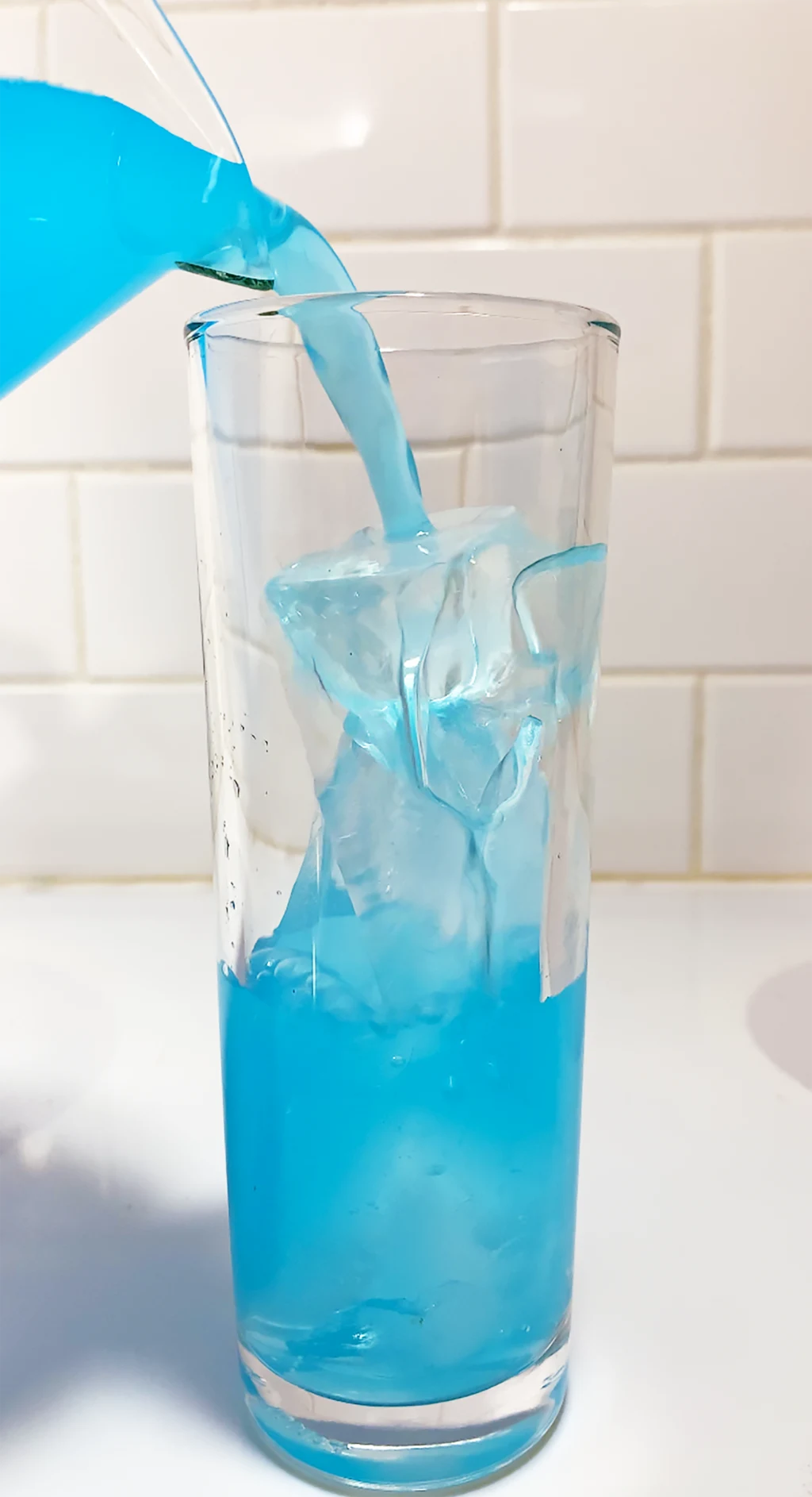 blue kool-aid being poured into a glass with ice