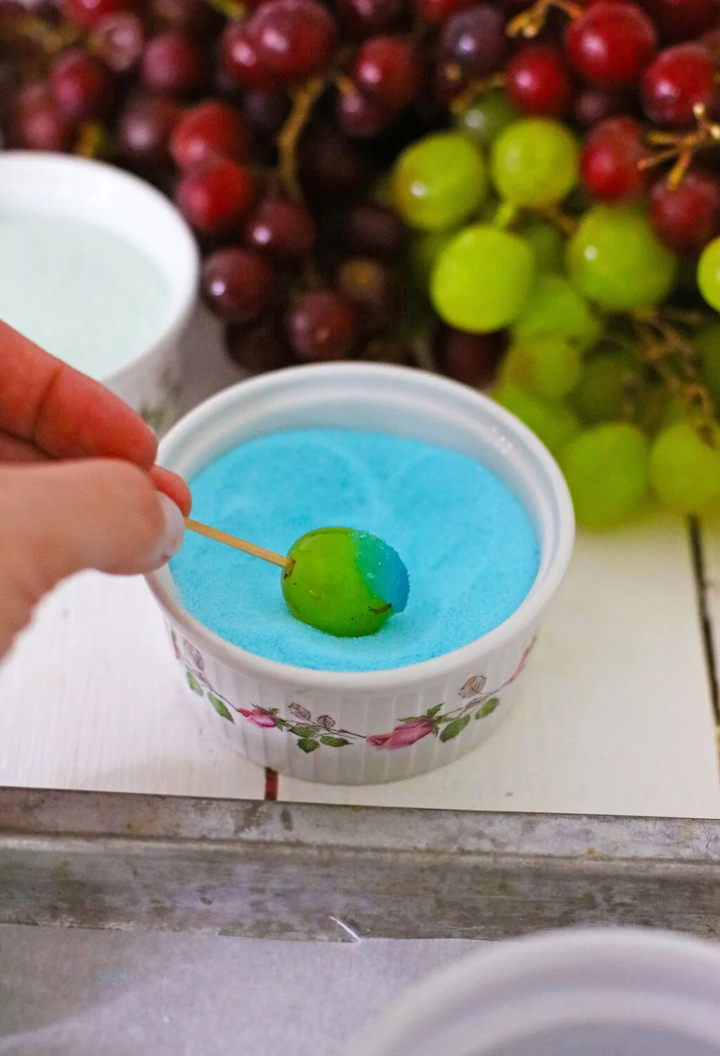 hand dipping grape into jello mixture