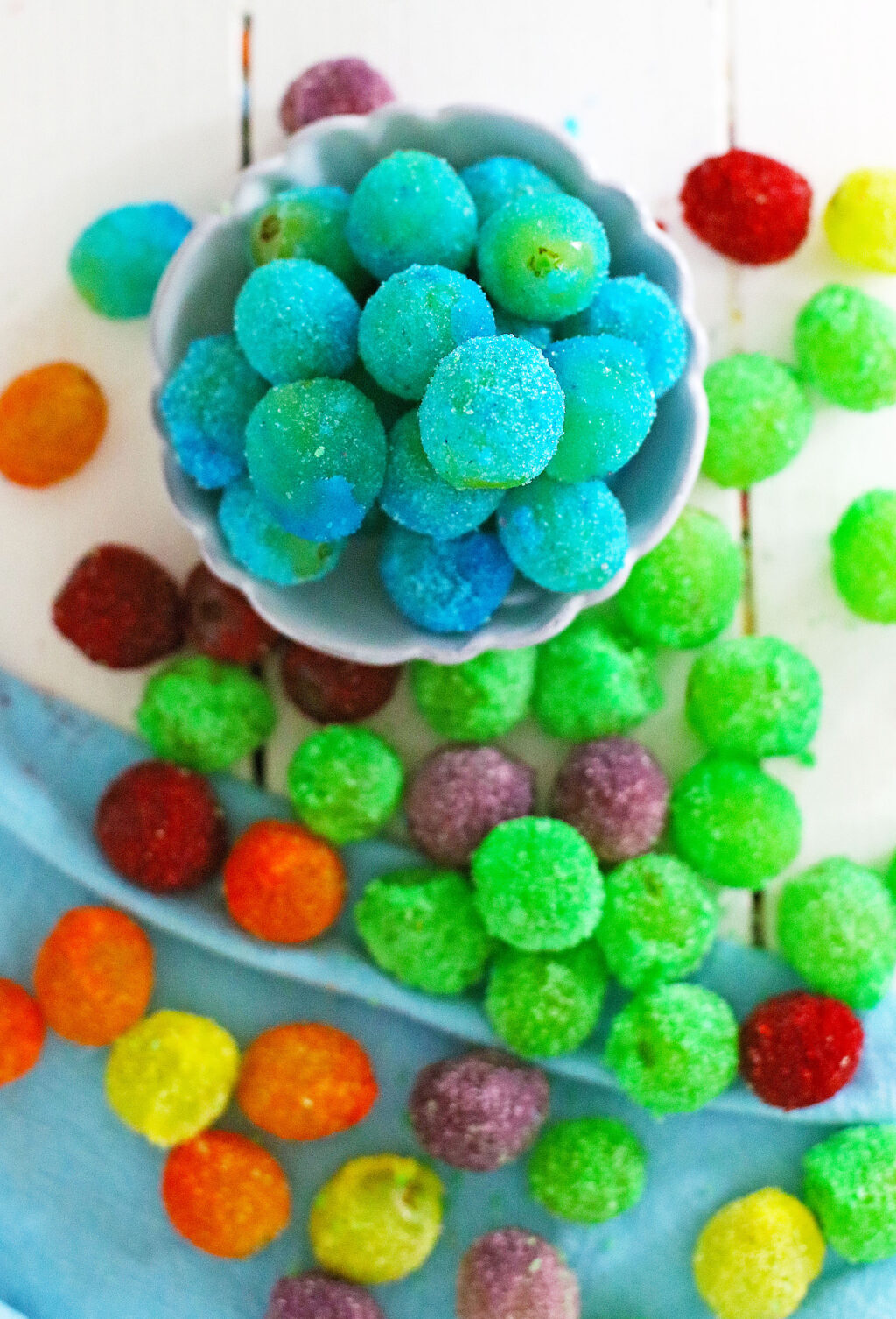 rainbow colored jello grapes on a white wood table and in a white round bowl