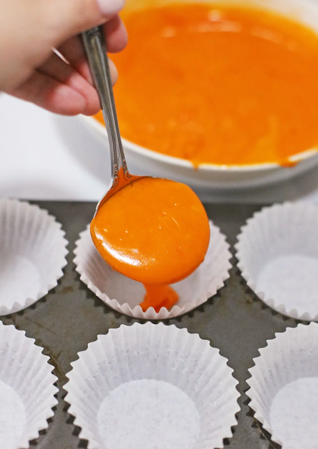 hand filling cupcake liners with orange cupcake batter