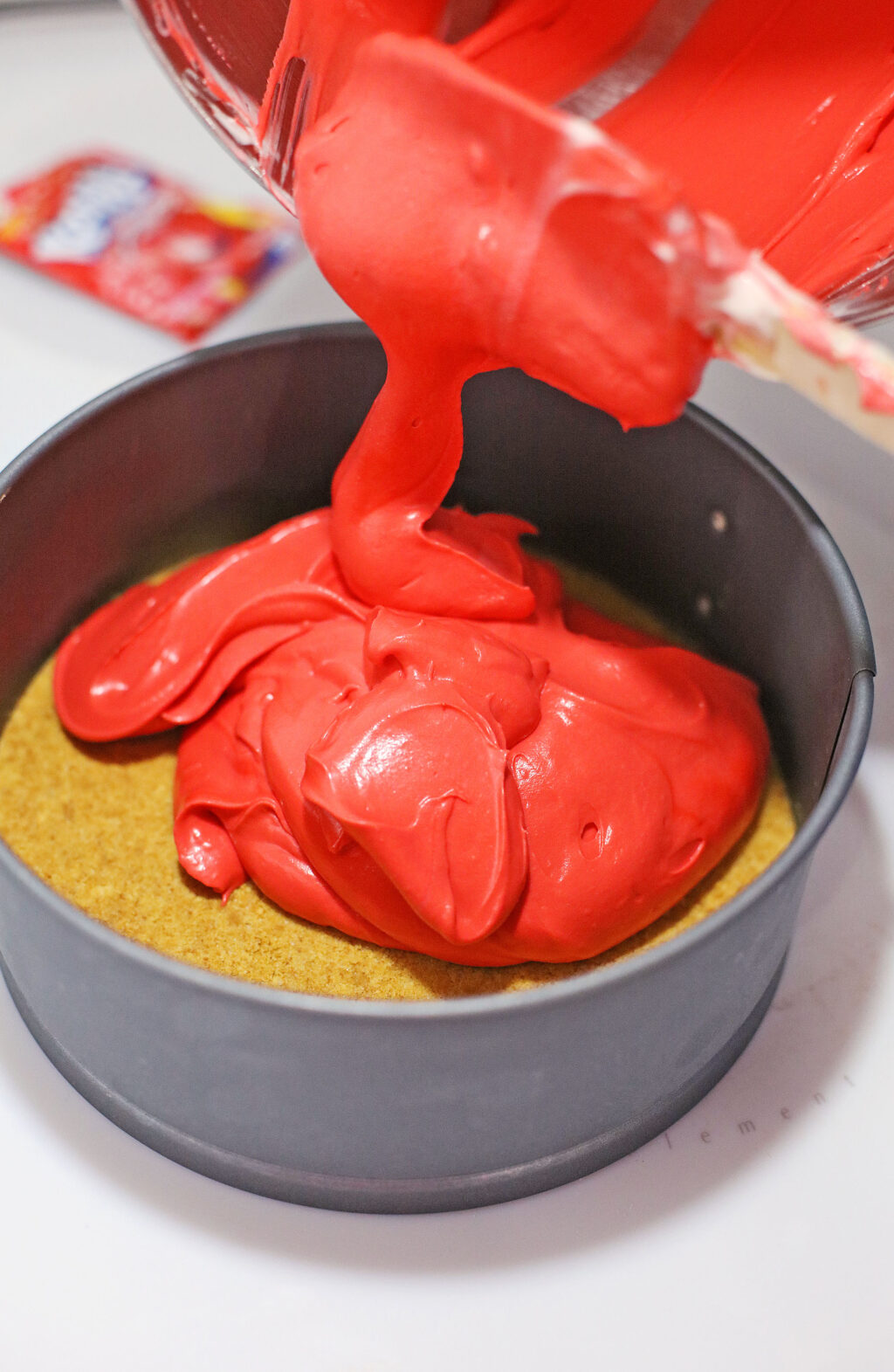 red koolaid cheesecake layer being poured over graham cracker crust
