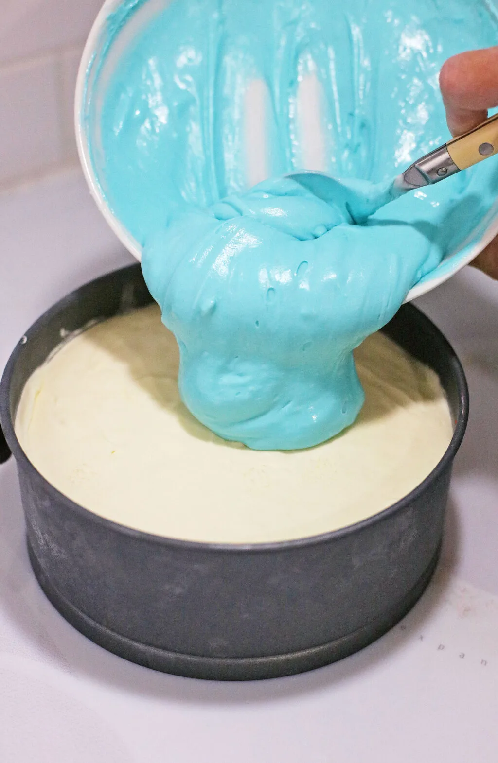 blue koolaid cheesecake layer being poured over graham cracker crust