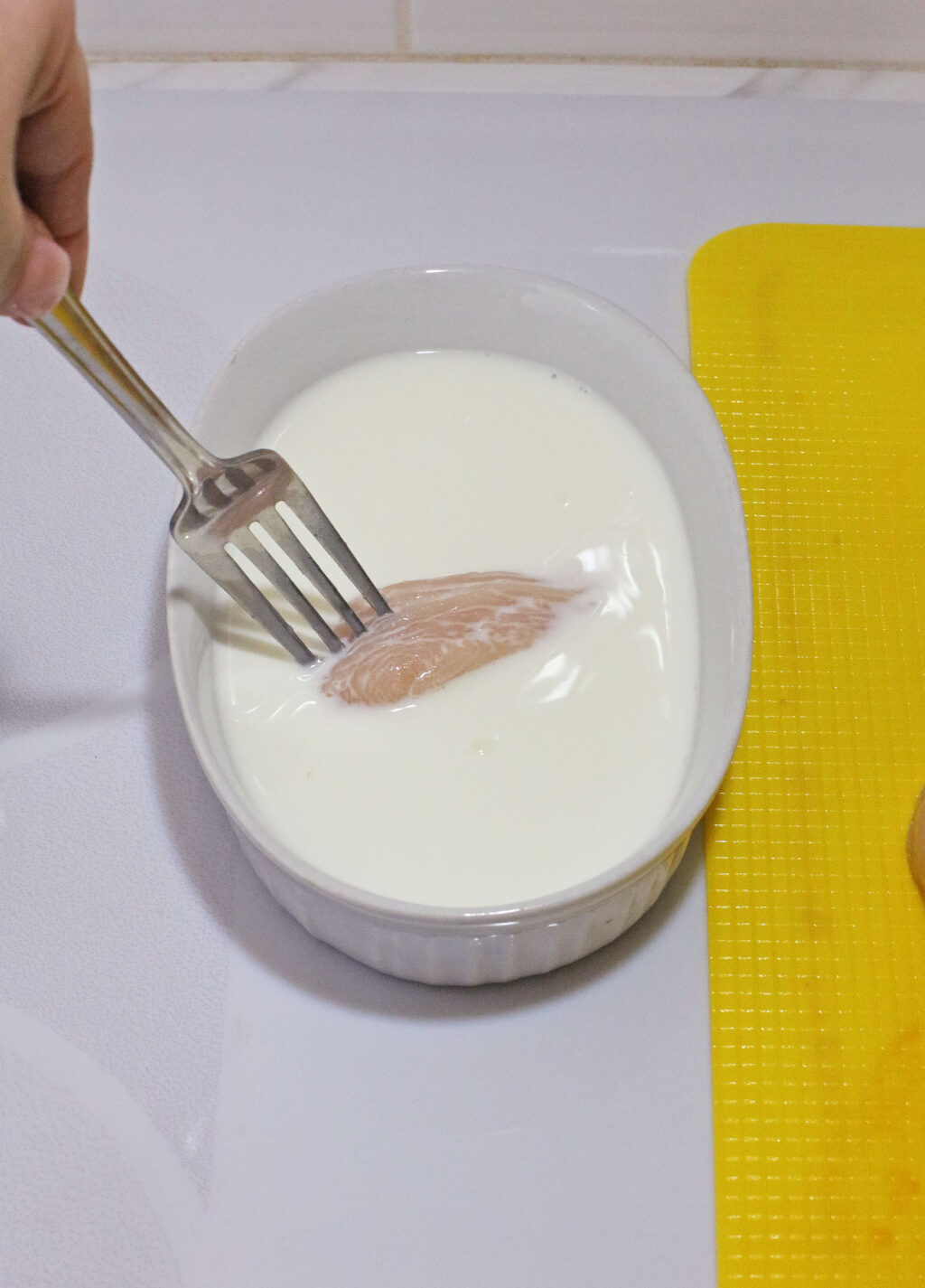 raw chicken nugget being dipped into milk