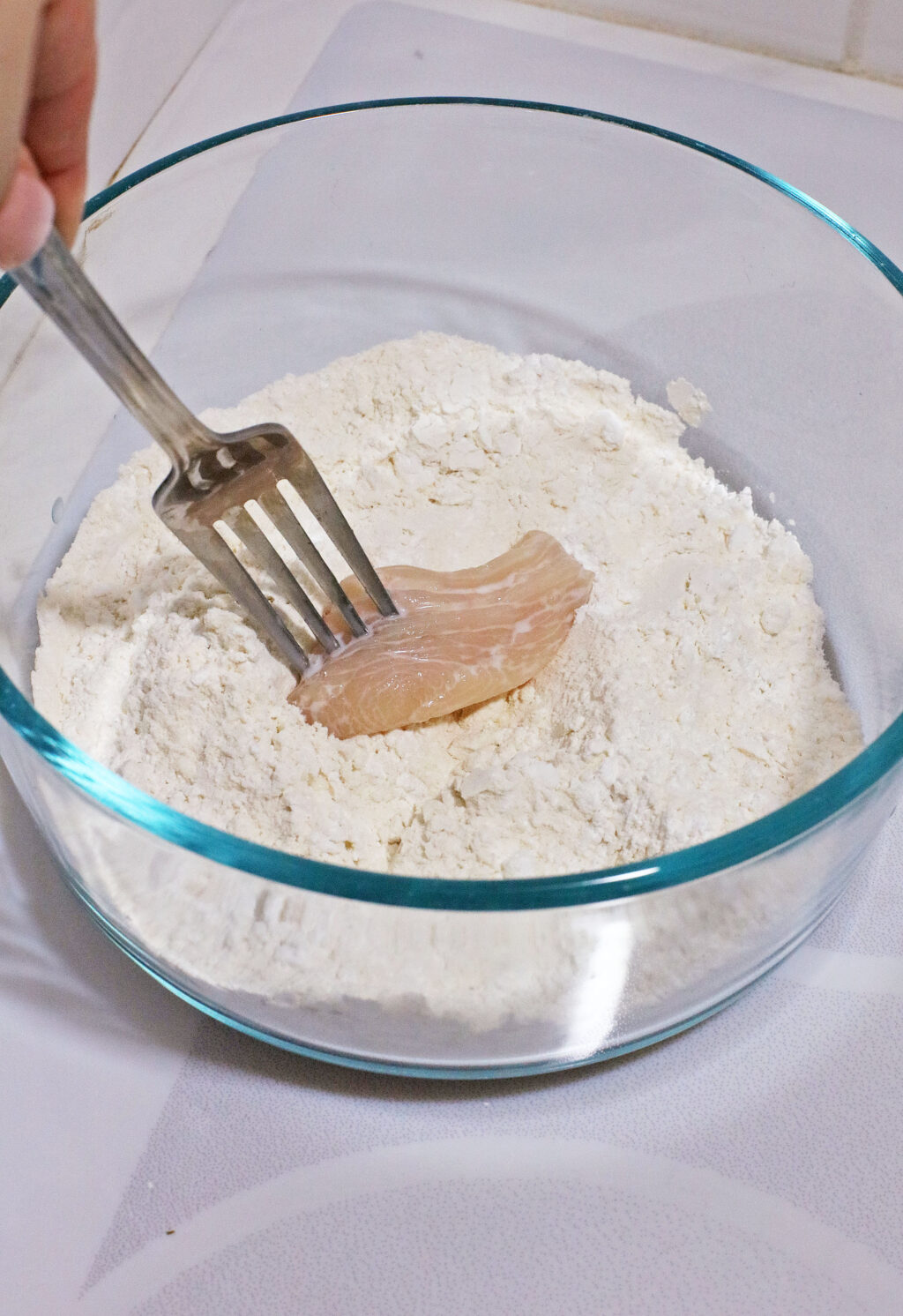 raw chicken nugget being dipped into flour mixture