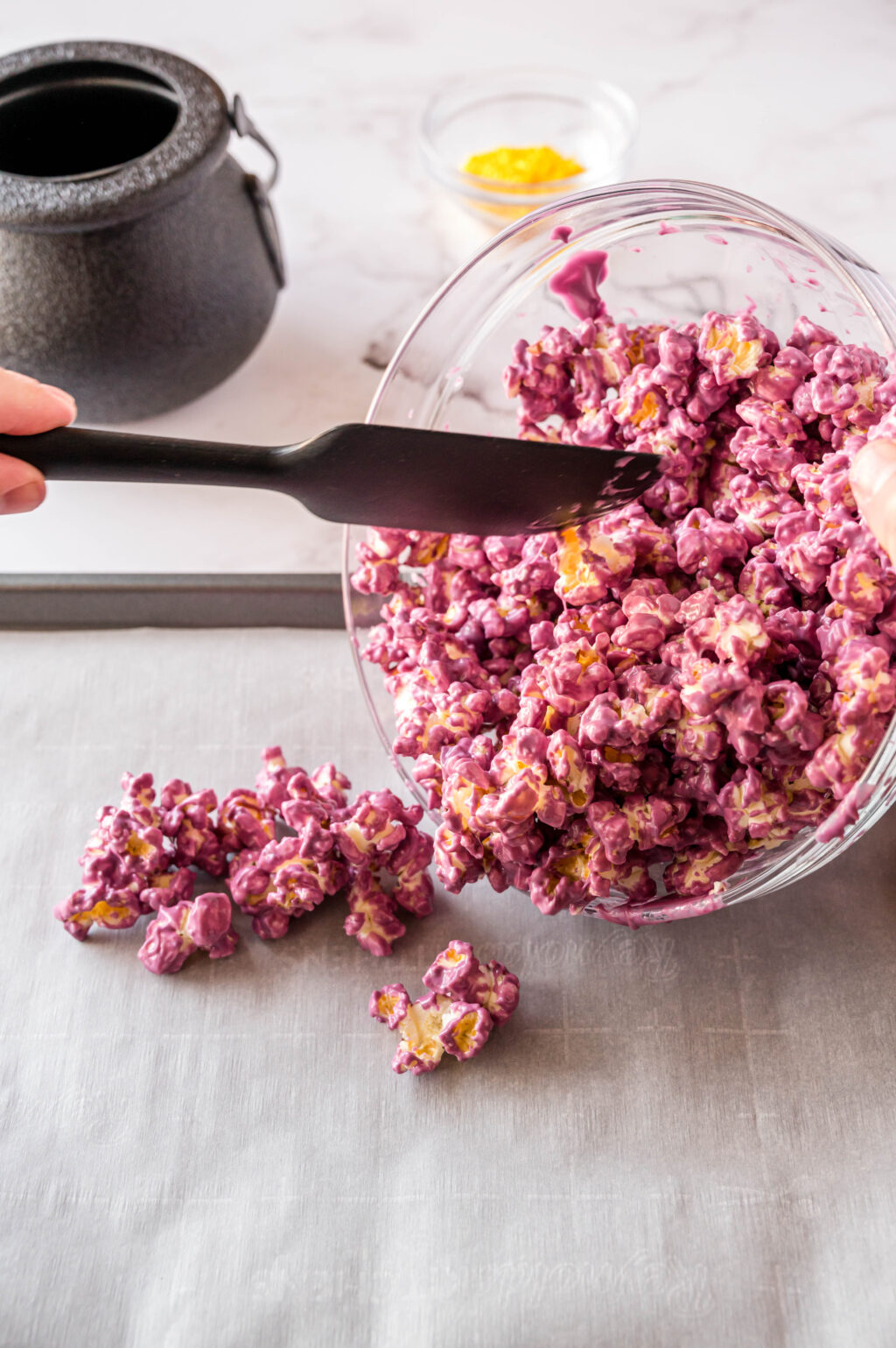 purple covered popcorn being poured onto cookie sheet