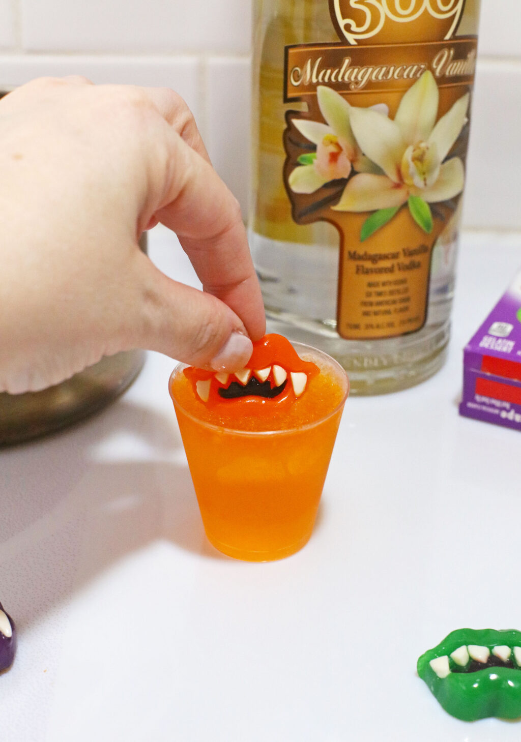 hand pushing monster teeth gummy into jello shot cup