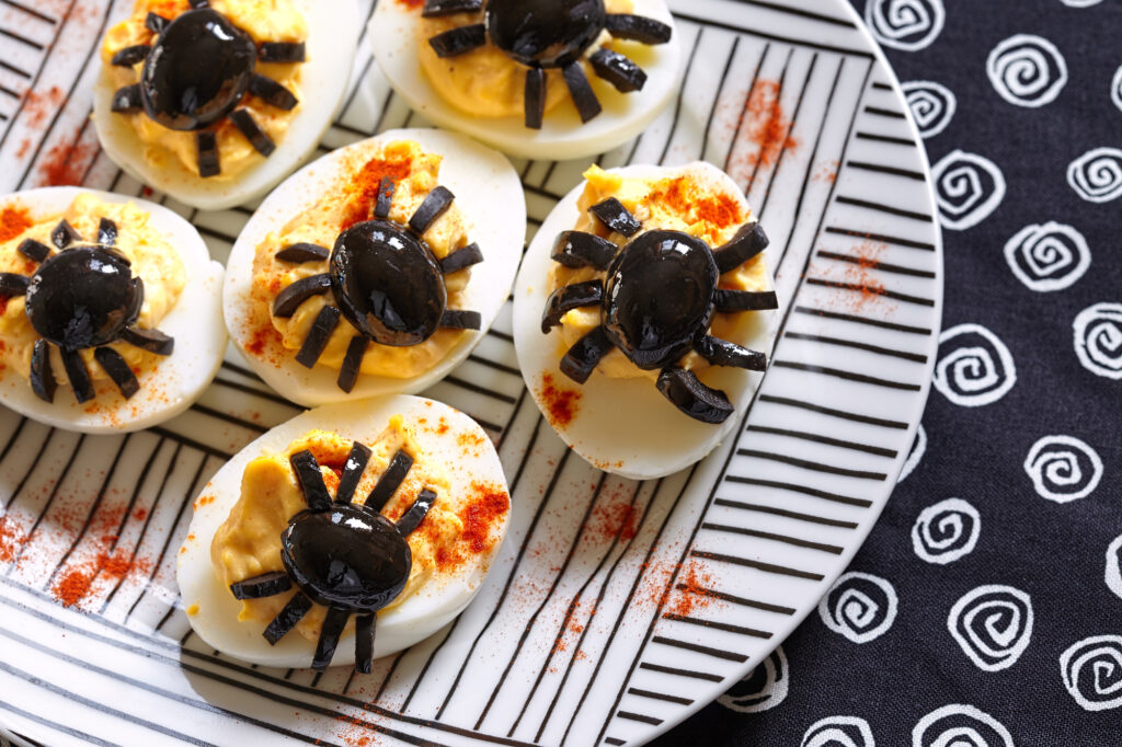 Deviled eggs with a Spider for Halloween on white and black striped plate